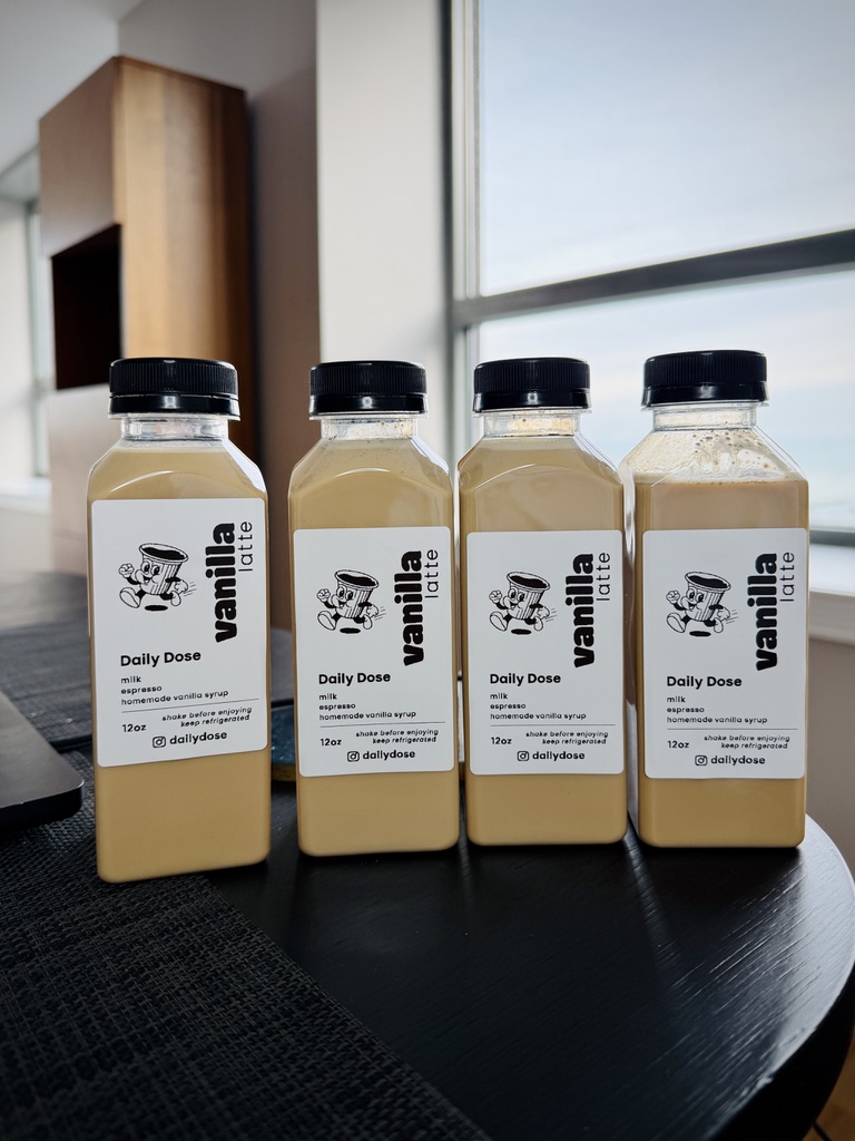 Four bottles of vanilla latte lined up on a table by the window